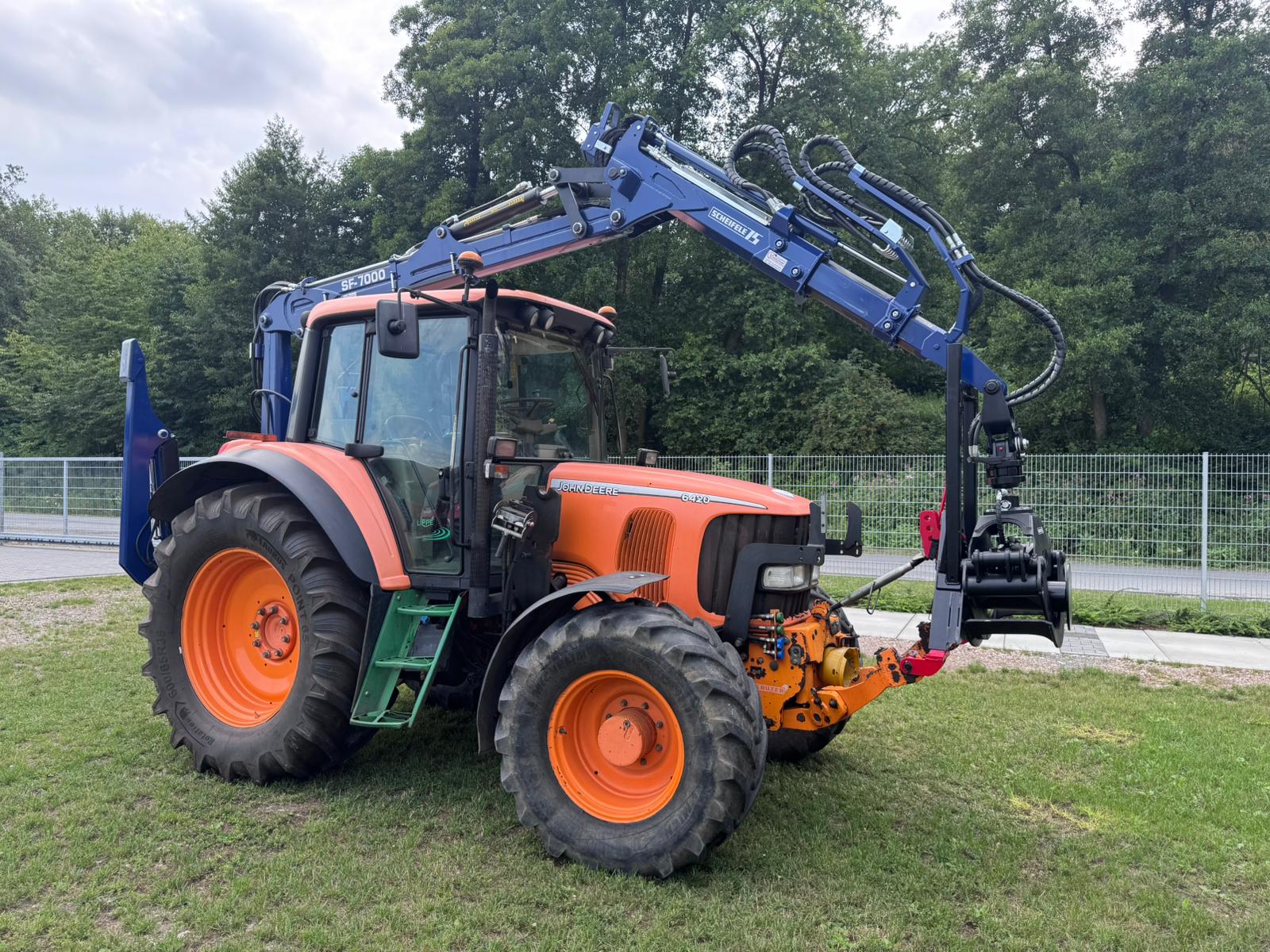 SF-7000 montiert auf Traktor Seitenansicht eines orangenen Traktors, der mit einem blauen Forstkran bestückt ist.