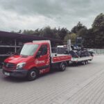 Ein roter Transporter von Deitmer zieht einen beladenen Anhänger.